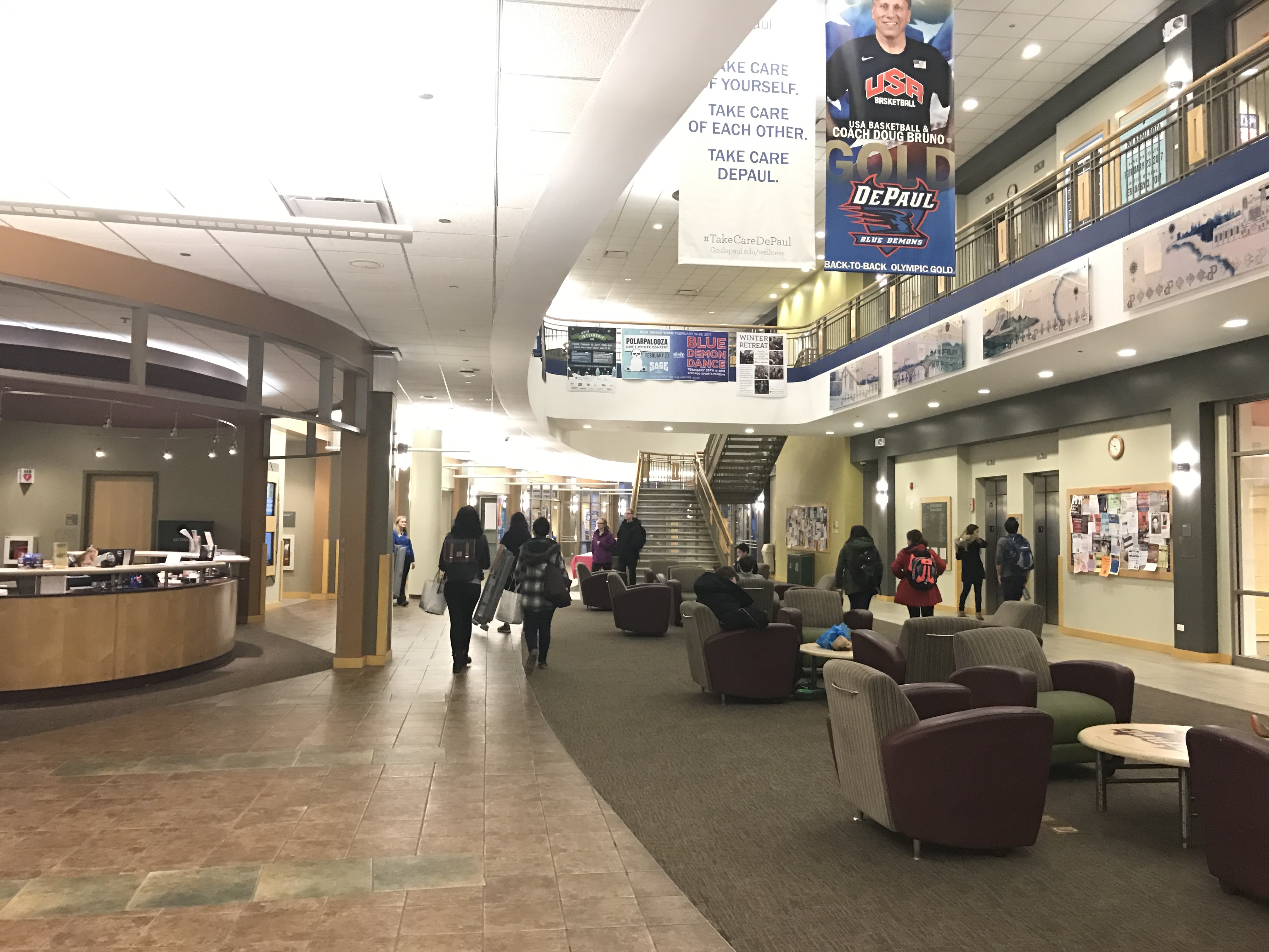 A large open area with an information desk, groups of chairs and tables, with stairs and elevators to upper floors. 