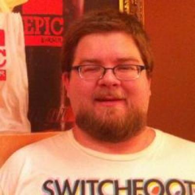 A rotund, bearded man with short, brown hair wearing a colorful T-shirt.