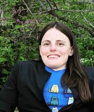 headshot of woman with long brown hair, blue a11y cats shirt and black blazer