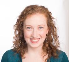 A woman with curly red hair wearing a deep green v-neck top smiling at the camera