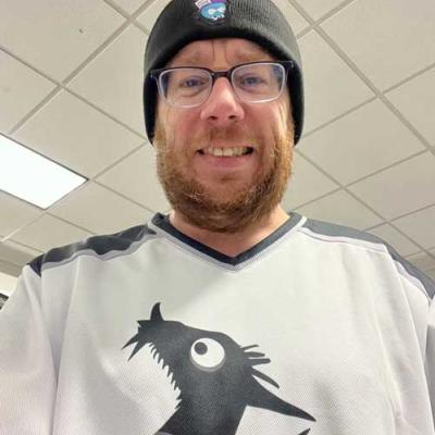 Man wearing glasses wearing a MidCamp hat and a Backdrop CMS hockey jersey